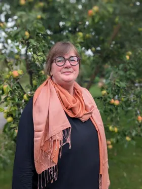Heike Suter mit Brille und orangem Schal im Garten
